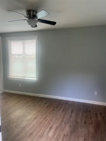 an empty room with wooden floor chandelier fan and windows