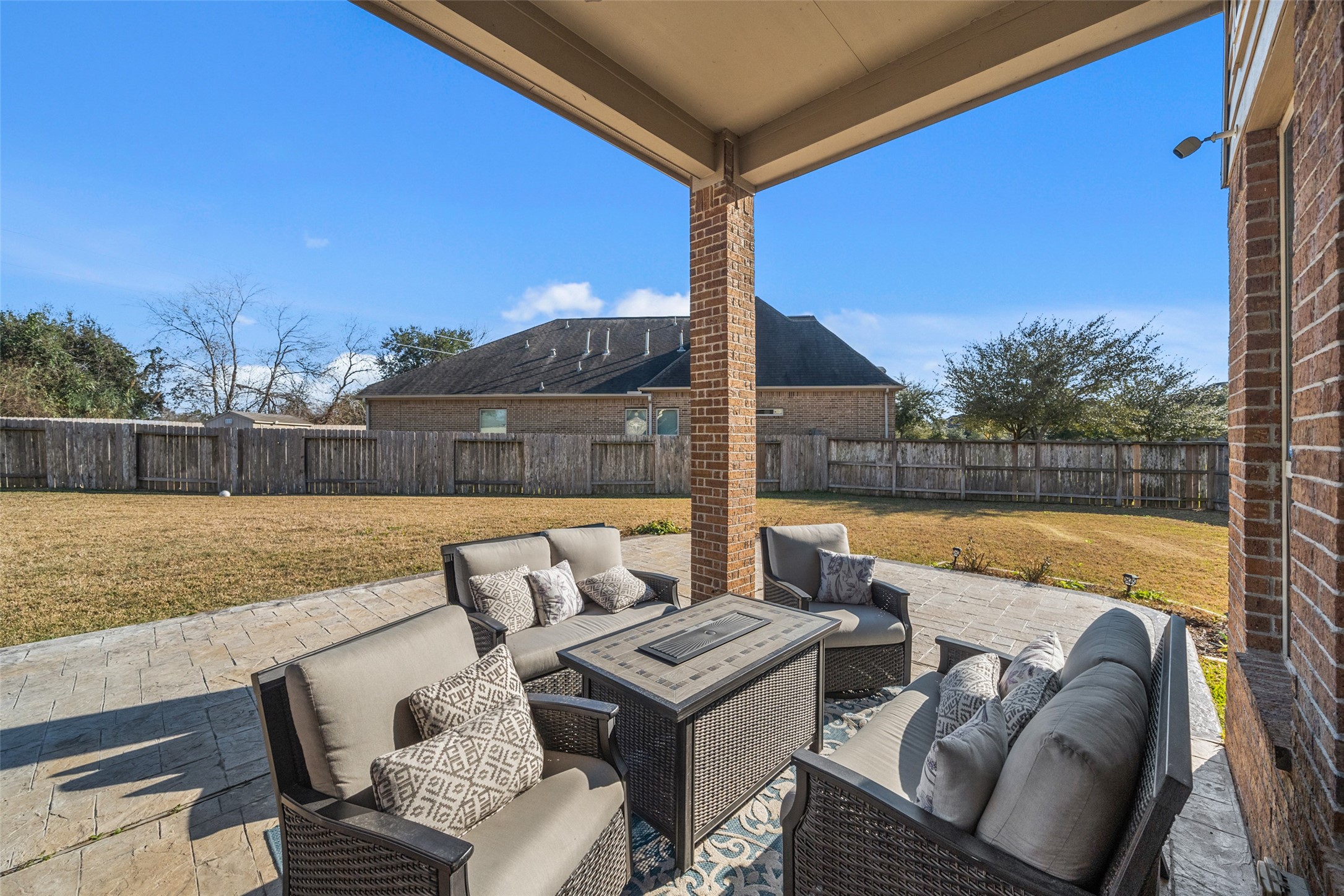 4747 Abercorn Street Rosharon, TX 77583 - Photo 34 of 46 This photo showcases a spacious backyard with a covered patio area featuring comfortable outdoor seating and a modern fire pit. The yard is fenced, offering privacy and ample space for outdoor activities, making it ideal for relaxation and entertaining.