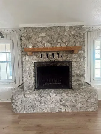 an empty room with wooden floor fireplace and window