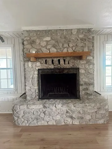 an empty room with wooden floor fireplace and window