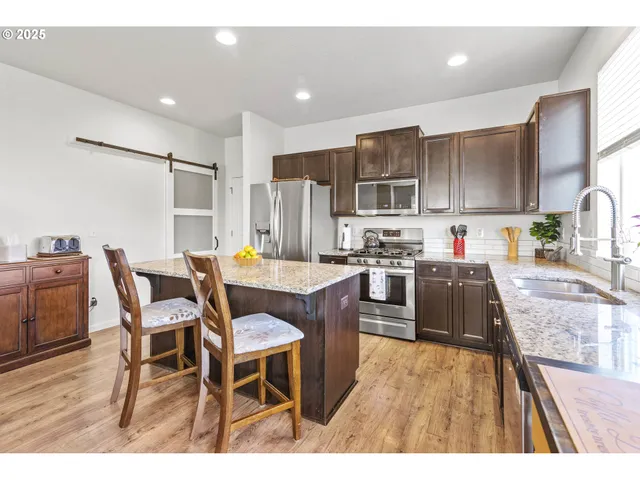 a kitchen with stainless steel appliances kitchen island granite countertop a table chairs and a refrigerator