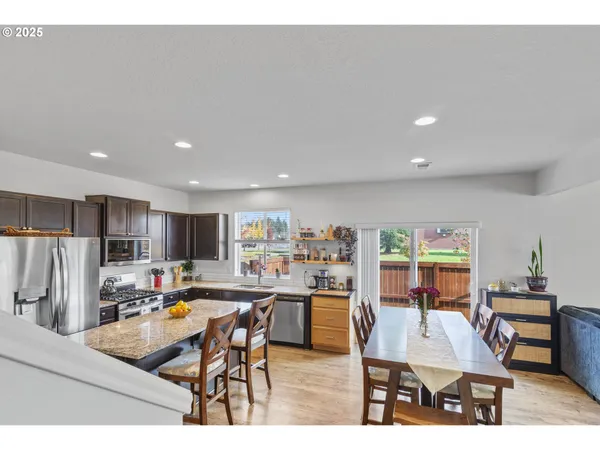 a kitchen with stainless steel appliances kitchen island granite countertop a refrigerator a stove a sink a dining table and chairs with wooden floor