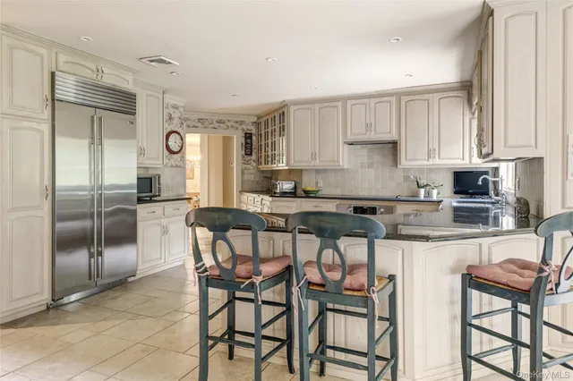 a kitchen with stainless steel appliances granite countertop a refrigerator a stove a sink and white cabinets with wooden floor