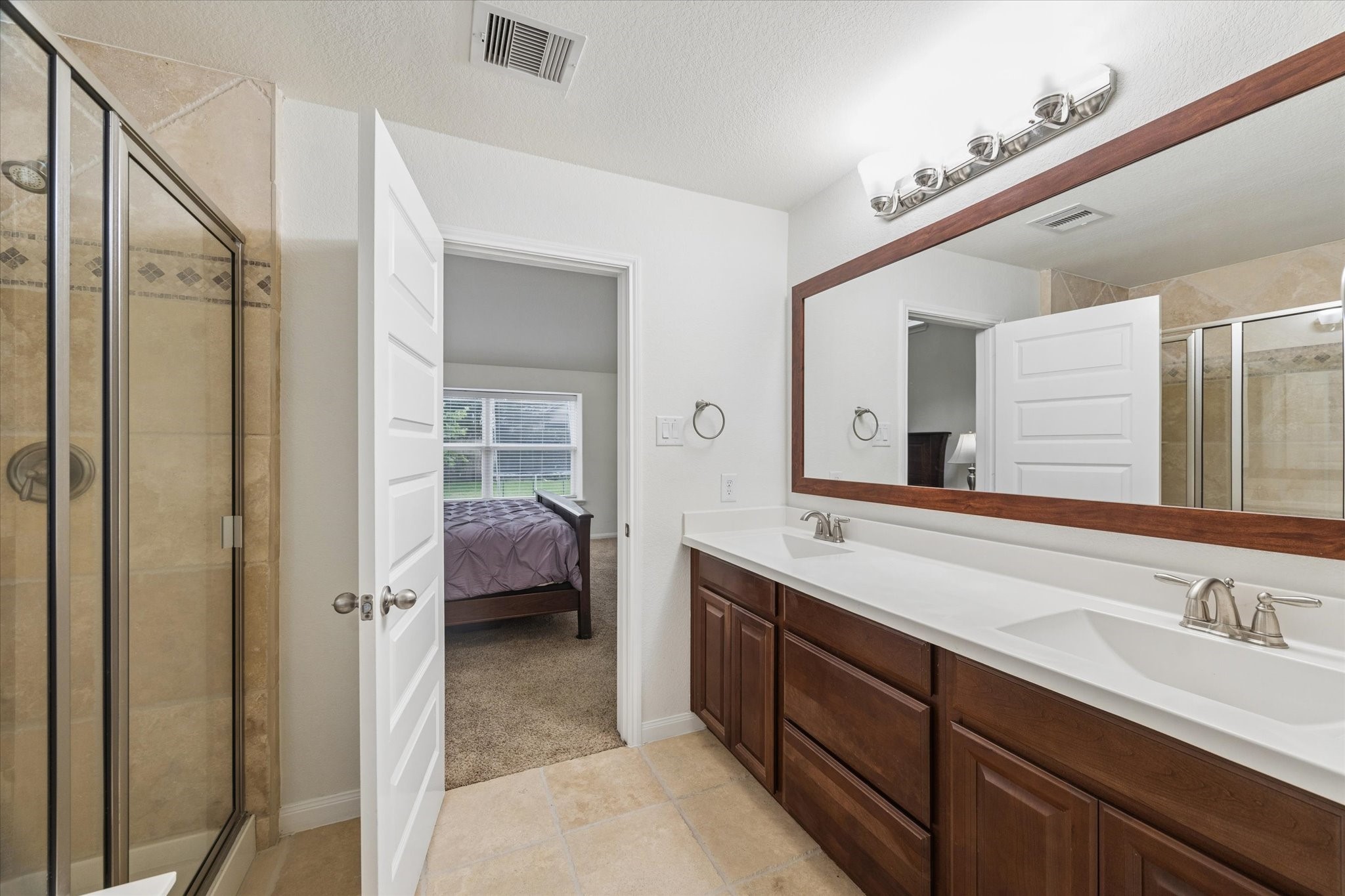 7015 Riata Hills Lane Spring, TX 77379 - Photo 18 of 33 This bathroom is clean, spacious, and thoughtfully designed with a long vanity offering ample counter space and storage. The oversized mirror and updated lighting keep the space bright and functional. A tiled walk-in shower with glass enclosure adds a polished touch, while neutral finishes make the room feel timeless and move-in ready.