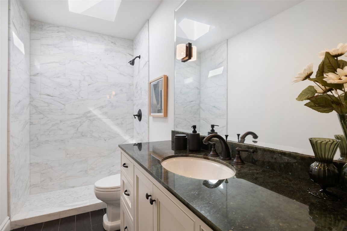 1810 West 35th Street Austin, TX 78703 - Photo 23 of 40 A skylight bathes this elegant bath in natural light, highlighting the marble shower, rich granite vanity, and timeless bronze fixtures.