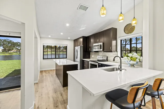 a kitchen with stainless steel appliances kitchen island granite countertop a stove a sink a microwave a dining table and chairs with wooden floor