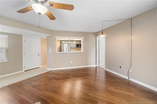 an empty room with wooden floor chandelier fan and windows