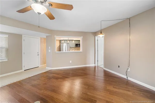 an empty room with wooden floor chandelier fan and windows
