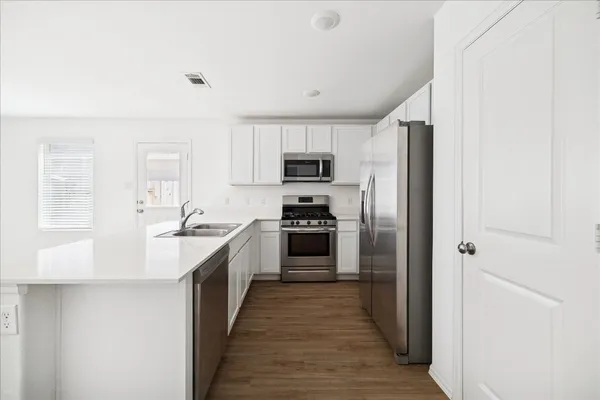 a kitchen with kitchen island granite countertop stainless steel appliances cabinets a sink and a wooden floor