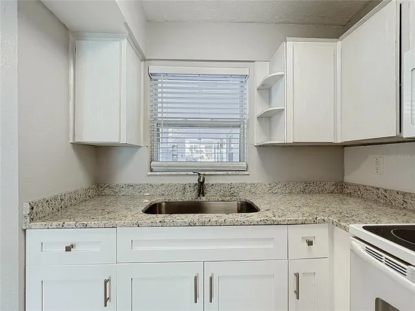 a kitchen with granite countertop white cabinets sink and window