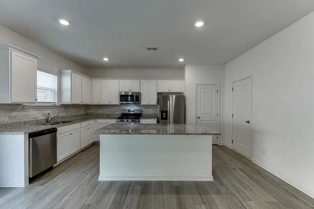 a large kitchen with stainless steel appliances granite countertop a stove a sink a refrigerator and a granite counter tops with wooden floors