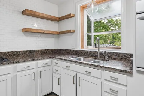 a kitchen with granite countertop white cabinets and a window