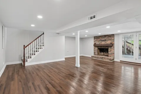 a view of an empty room with wooden floor fireplace and a window