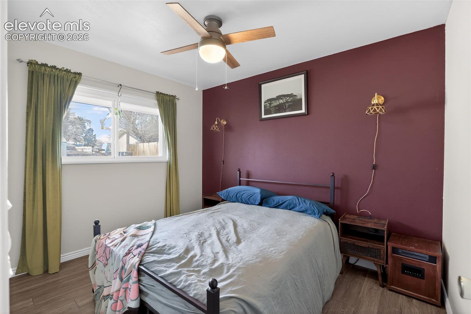 Bedroom featuring wood-finish flooring, a ceiling fan with integrated lighting, and a white-framed window