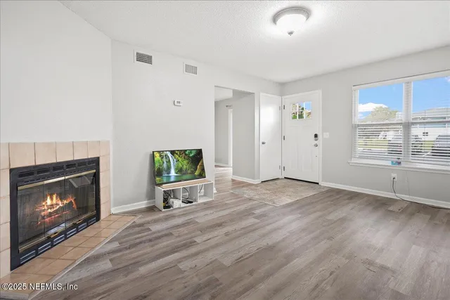 a view of an empty room with wooden floor fireplace and a window