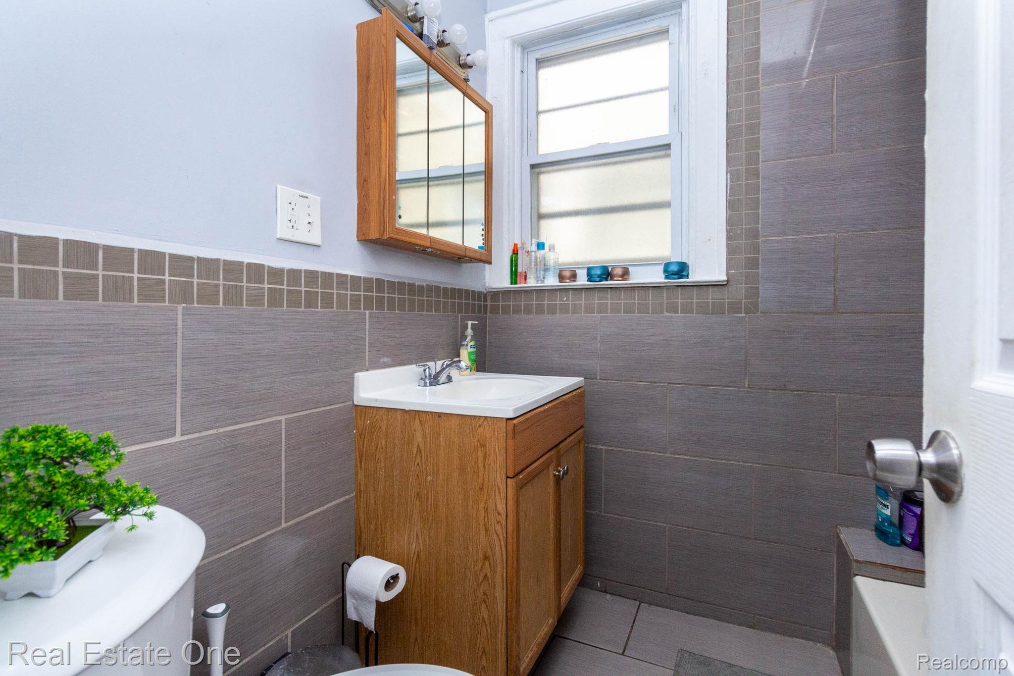 5485 Springwells Street Detroit, MI 48210 - Photo 12 of 47 Bathroom featuring a vanity with a white countertop and wood-finish cabinetry, a built-in medicine cabinet with mirror, large format grey wall tiling, and a window with white trim