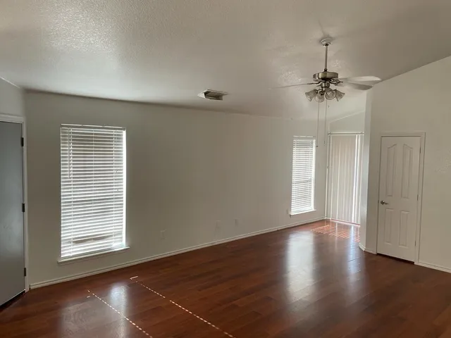 an empty room with wooden floor chandelier fan and windows