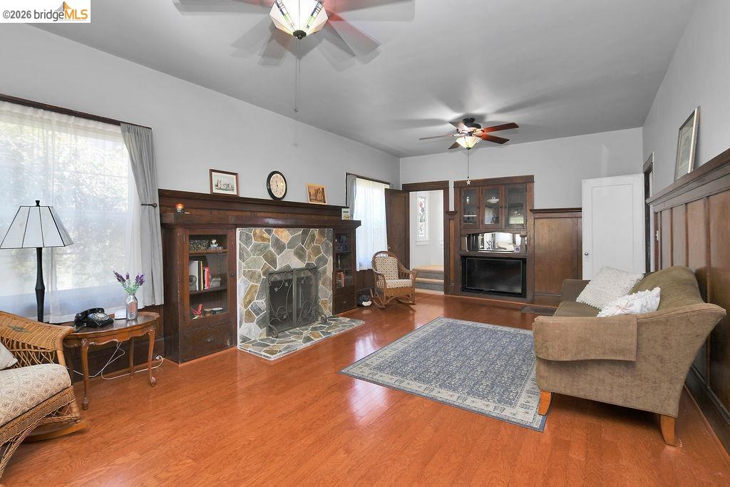 325 South 2nd Street Rio Vista, CA 94571 - Photo 9 of 33 Living room featuring wood-finish flooring, a stone-faced fireplace with built-in shelving, two ceiling fans, and dark wood wainscoting