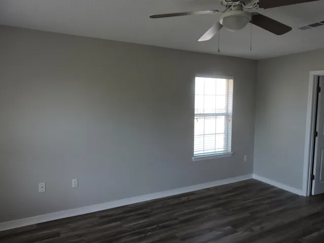 an empty room with wooden floor fan and windows