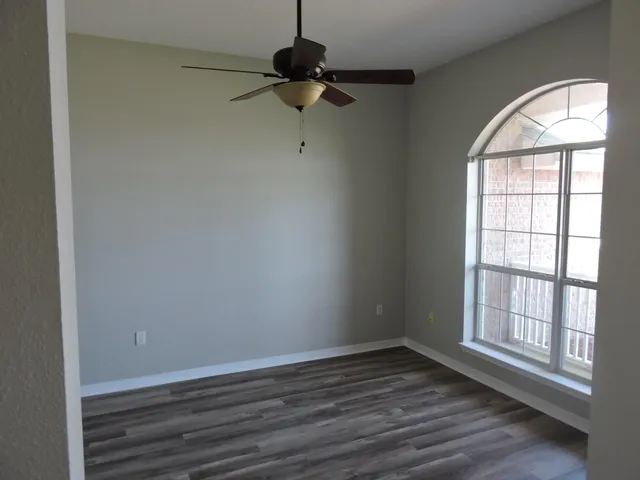 an empty room with wooden floor fan and windows