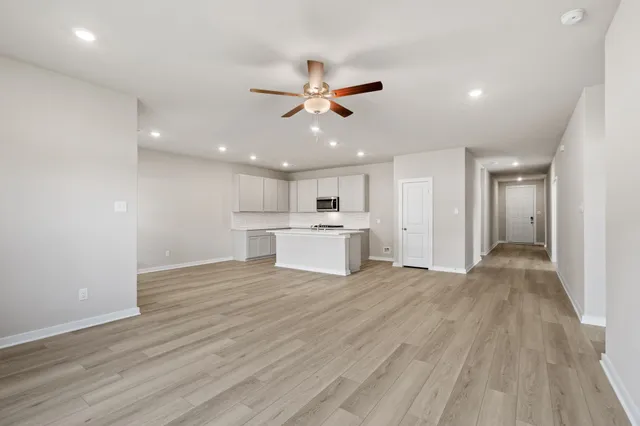 a view of an empty room with wooden floor and a ceiling fan