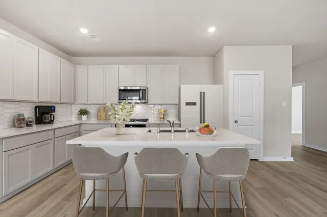 a kitchen with stainless steel appliances a stove a sink a refrigerator white cabinets and wooden floor