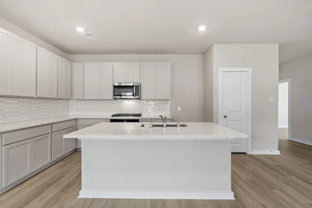 a kitchen with stainless steel appliances granite countertop a sink a stove a refrigerator with white cabinets and wooden floor