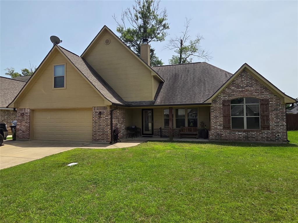 Traditional-style house featuring brick siding, a front lawn, covered porch, driveway, and an attached garage