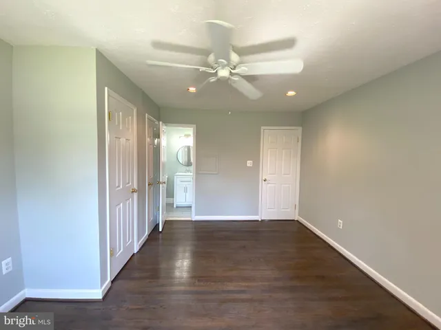 a view of an empty room with wooden floor and a ceiling fan