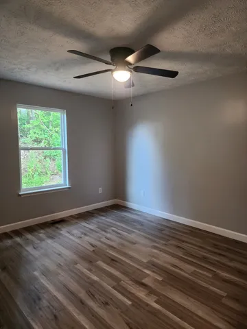 an empty room with wooden floor chandelier fan and windows