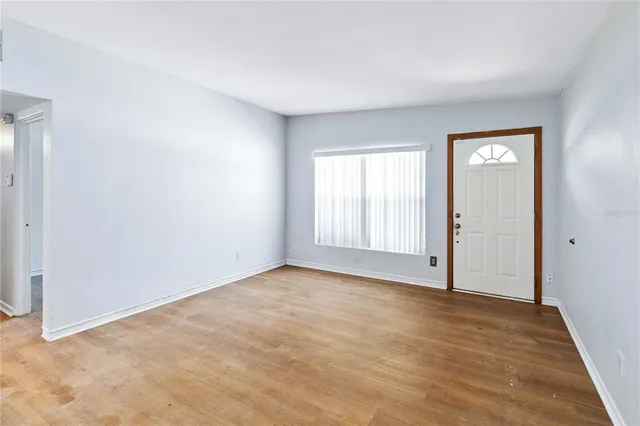 a view of an empty room with wooden floor and a window