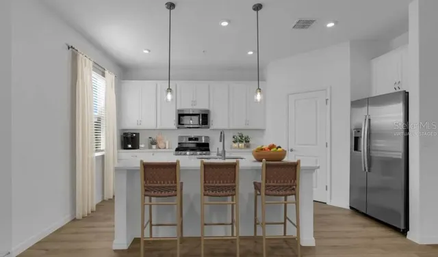 a kitchen with stainless steel appliances a dining table chairs refrigerator and microwave