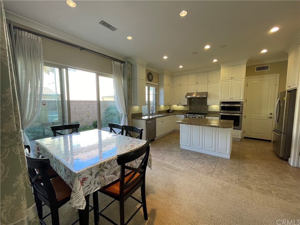 71 Thornapple Irvine, CA 92620 - Photo 13 of 18 a kitchen with stainless steel appliances granite countertop a stove top oven a sink dishwasher a dining table and chairs with wooden floor