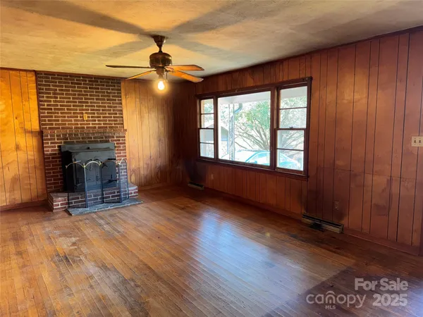 an empty room with wooden floor fireplace and windows