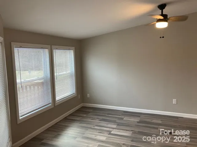 an empty room with wooden floor fan and windows