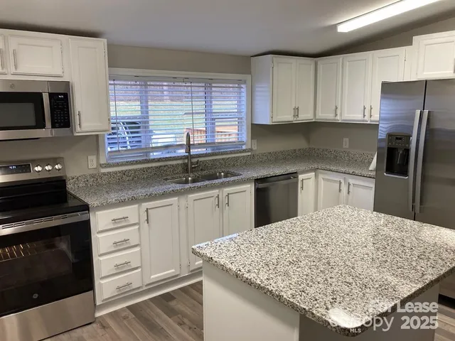 a kitchen with granite countertop a sink stainless steel appliances and white cabinets