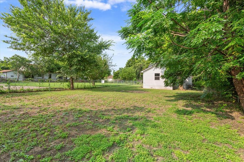 3109 North 20th Street Waco, TX 76708 - Photo 22 of 24 Expansive green space featuring a white siding structure with a dark-framed window, surrounded by mature trees and partially enclosed by a chain-link fence
