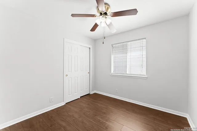 an empty room with wooden floor ceiling fan and windows