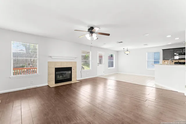 a view of a room with wooden floor a ceiling fan and kitchen view