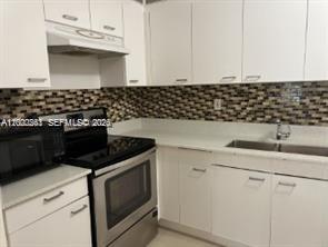 9341 Collins Avenue, Unit 604 Surfside, FL 33154 - Photo 7 of 15 a kitchen with granite countertop white cabinets and black appliances