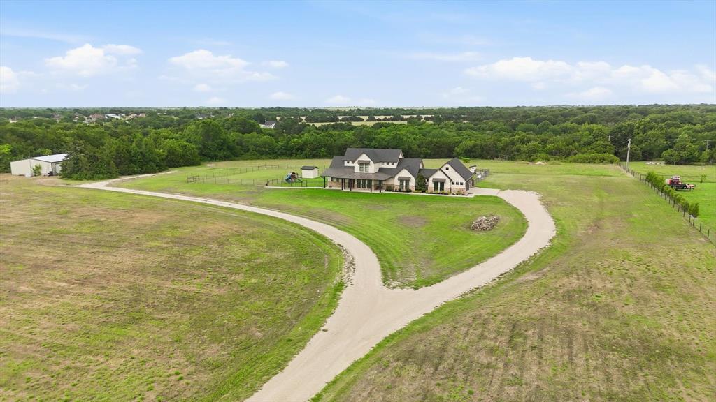 6020 Honeysuckle Road Midlothian, TX 76065 - Photo 36 of 39 Spacious rural property featuring a large residence with an expansive covered front porch, a separate metal-roofed outbuilding, and a winding gravel driveway