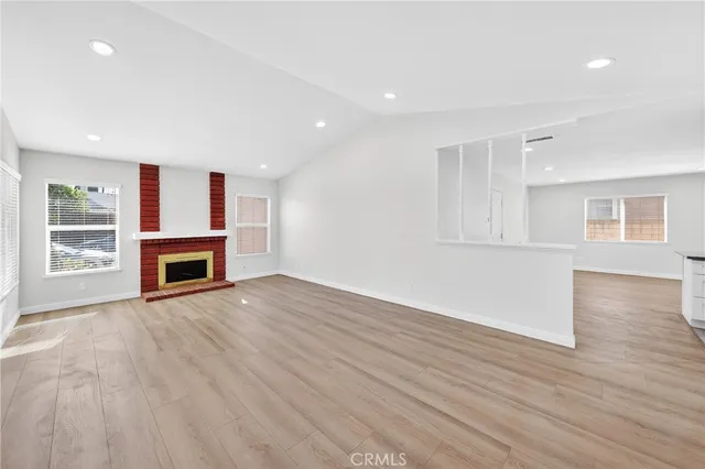 an empty room with wooden floor fireplace and windows