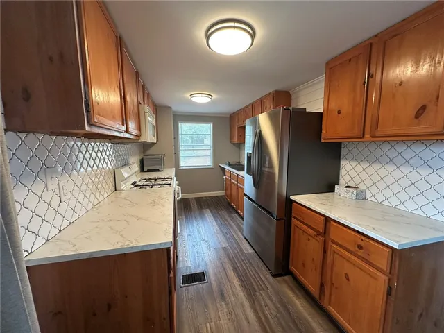 a kitchen with granite countertop a refrigerator a stove a sink dishwasher and wooden cabinets with wooden floor