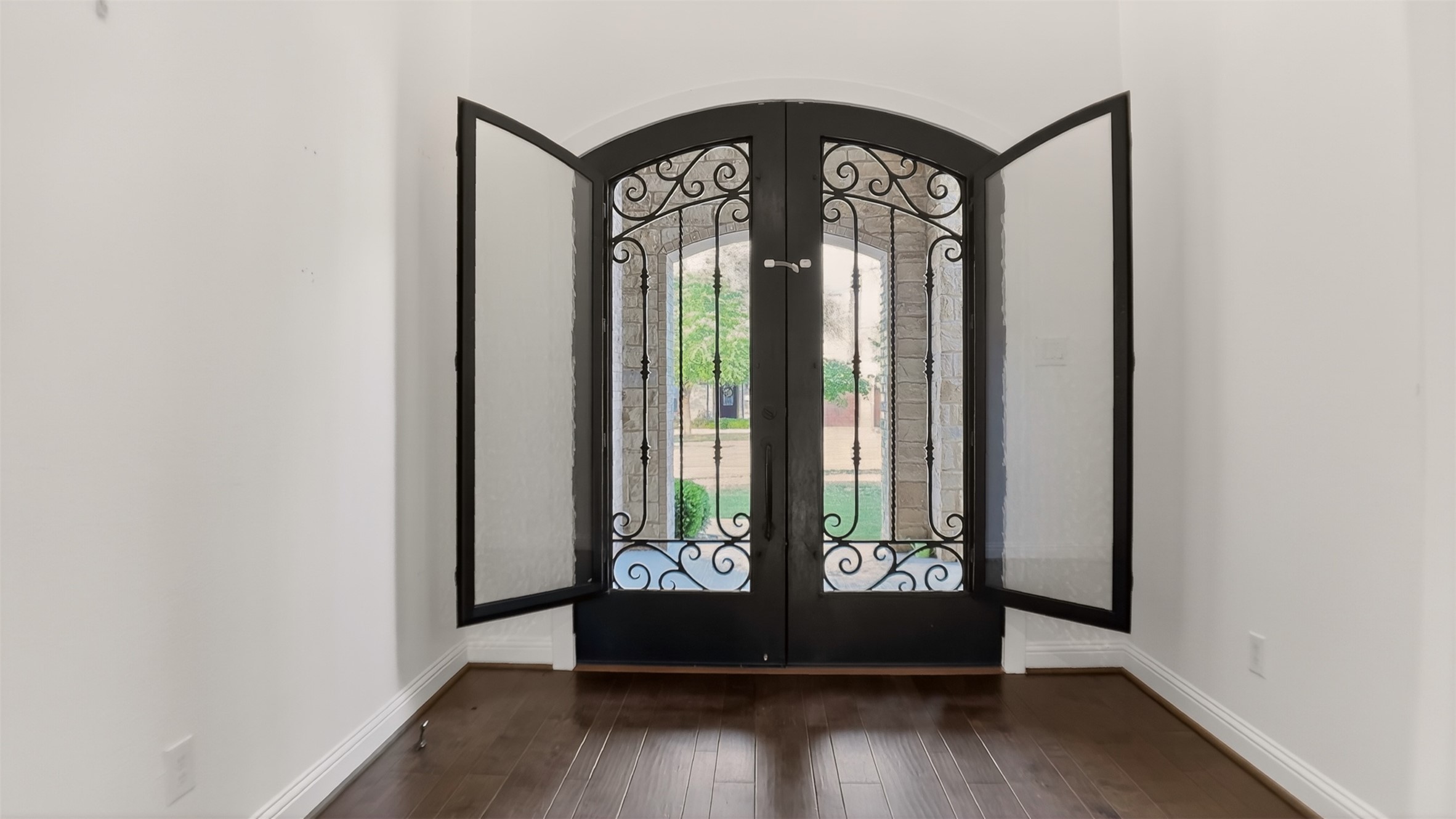 1505 Long Shadow Lane Georgetown, TX 78628 - Photo 3 of 28 Arched double entry doors with intricate wrought iron detailing, dark wood-finish flooring, white baseboards, and white wall finishes