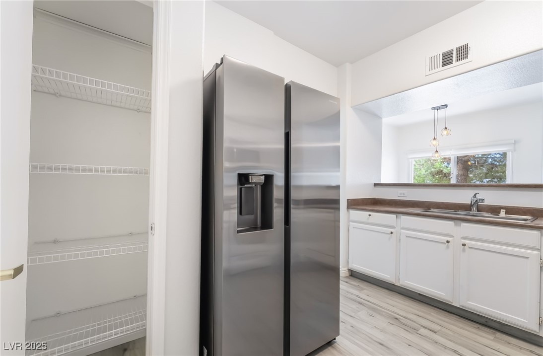 7255 West Sunset Road, Unit 1148 Las Vegas, NV 89113 - Photo 20 of 62 Kitchen featuring stainless steel refrigerator with ice dispenser, light wood finished floors, white cabinetry, hanging light fixtures, and dark countertops