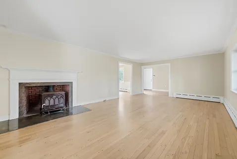 a view of an empty room with wooden floor fireplace and a window