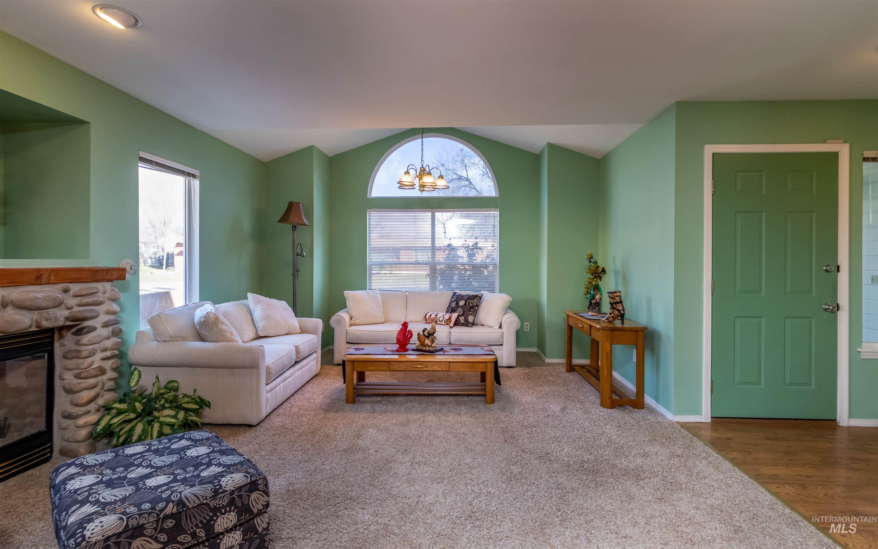 1811 Cleveland Street Boise, ID 83705 - Photo 7 of 30 Carpeted living area featuring lofted ceiling, a chandelier, a stone fireplace, plenty of natural light, and wood finished floors