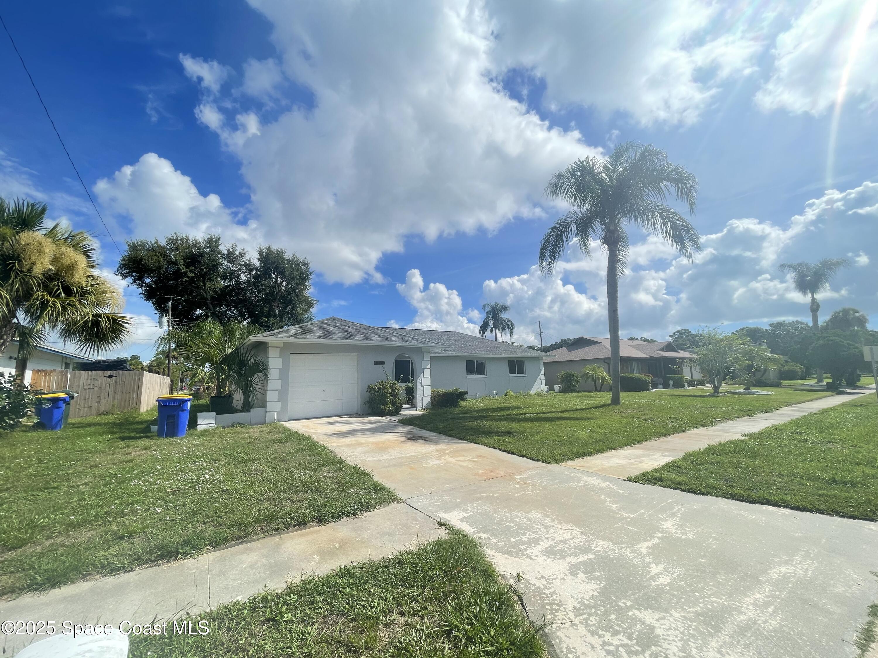 1118 Manatee Drive Rockledge, FL 32955 - Photo 2 of 17 a view of a white house in front of a big yard with plants and large trees
