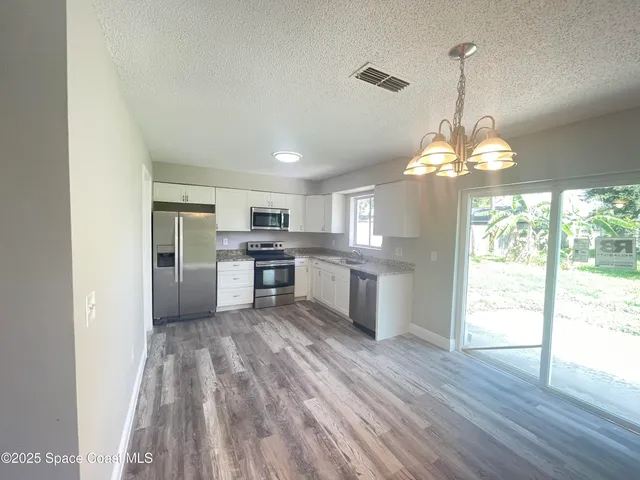 a kitchen with stainless steel appliances granite countertop a refrigerator a sink dishwasher a stove and white countertops with wooden floor