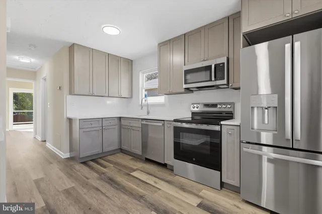 a kitchen with stainless steel appliances granite countertop a refrigerator stove a sink and white cabinets with wooden floors